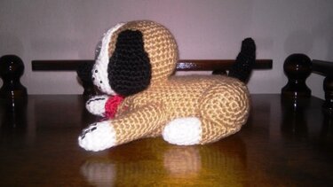 Amigurumi liegender Hund, beiger Körper, weiße Pfoten, schwarze Ohren, schwarzer Schwanz, rotes Halsband