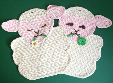 Zwei gehäkelte Schaf-Topflappen, cremefarbener Körper, rosa Gesichter, mit kleinen Blütenapplikationen