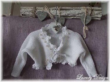 Weiße gestrickte Babyjacke mit Häkelspitze, Perlen und Bindeschleife an Aufhänger