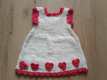 cremeweißes Strickkleid mit rosa Rüschen an Ärmeln und Saum und fünf rosa Herz-Applikationen entlang des Saums