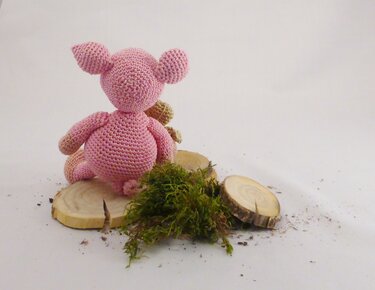 Rückansicht eines rosa gehäkelten Amigurumi-Schweins auf Holzscheiben mit Moos