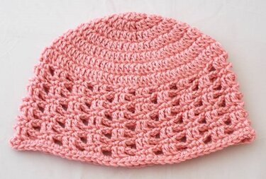Rosa gehäkelte Babymütze mit Lochmuster auf hellem Hintergrund