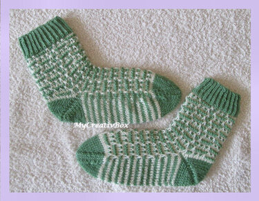 Paar gestrickter Kindersocken in Grün und Weiß mit Rippenbündchen und gestreiftem Fuß