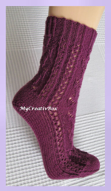 Einzelne beerenfarbene gestrickte Socke mit durchbrochenem Lochmuster am Schaft, getragen an einem Fuß vor hellem Hintergrund.