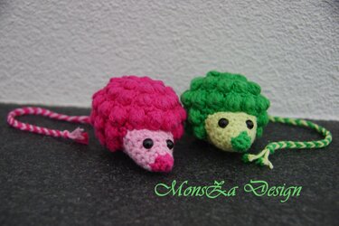Zwei gehäkelte Mini-Igel-Schlüsselanhänger, einer pink und einer grün, mit geflochtenen Bändern