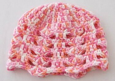 Gehäkelte Mütze für Babys in Rosa, Orange und Weiß mit Lochmuster und gewelltem Rand.