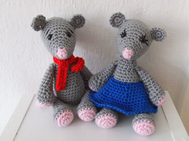 Zwei graue gehäkelte Amigurumi‑Mäuse, eine mit rotem Schal, die andere mit blauem Rock
