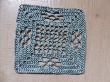 Gehäkeltes Granny Square in Minzgrün mit offenem Gittermuster auf hellem Holzuntergrund