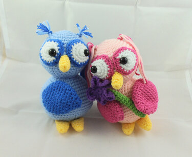 Rosa und blaue gehäkelte Eulen-Amigurumi, eine hält eine lila Häkelblume