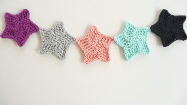 Fünf bunte gestrickte Sterne als Applikationen auf hellem Hintergrund