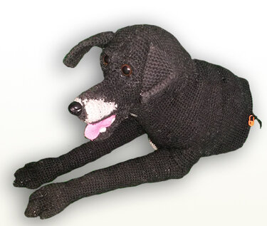 Gehäkelter schwarzer Amigurumi-Hund, liegend, mit weißer Schnauze und herausgestreckter Zunge