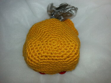 Gelbes gehäkeltes Hähnchen-Spielzeug mit silbernem Foliendetail auf hellem Hintergrund