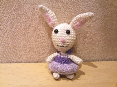 Weißer gehäkelter Amigurumi-Hase mit lila Kleid, rosa Innenohren und schwarzen Knopfaugen