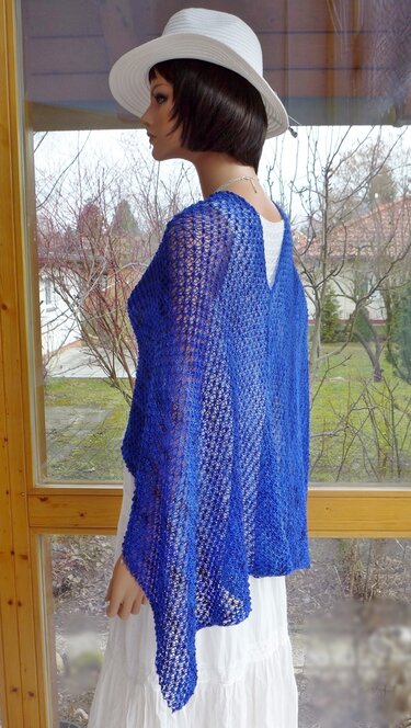 Mannequin mit weißem Hut trägt blauen, offenen Strickponcho über weißem Kleid; Seitenansicht mit V-Rücken