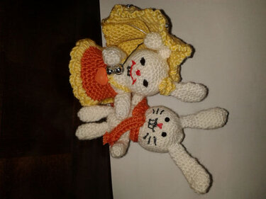 Zwei weiße gehäkelte Hasen, einer mit gelbem Hut und Glocke, der andere mit orangefarbenem Schal.