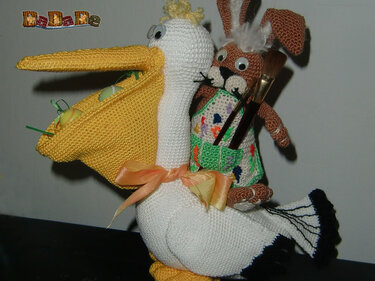 gehäkelter weißer Storch mit gelbem Schnabel und braunem Amigurumi-Hasen, kleine Ostereier und Pinsel
