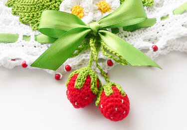 Zwei rote, gehäkelte Erdbeeren mit grünen Blättern und grüner Schleife auf hellem Hintergrund.