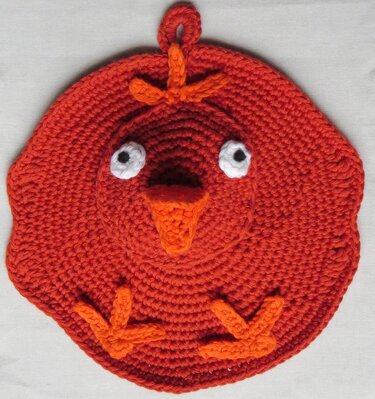 Runder gehäkelter Topflappen in Hühnerform, orange mit weißen Augen und orangenem Schnabel.