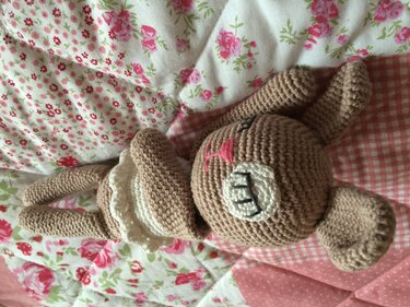 Niedlicher gehäkelter Hase mit gesticktem Gesicht und weißer Rüschenkante auf geblümter Decke