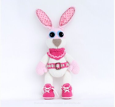 Gehäkelter weiß-rosa Amigurumi-Hase mit gepunkteten Ohren und pinken Schnürschuhen auf hellem Hintergrund