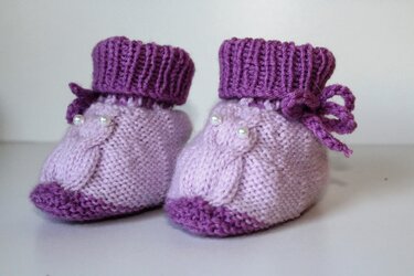 Lila gestrickte Babyschuhe mit Zopfmuster, Perlen und geripptem Umschlag