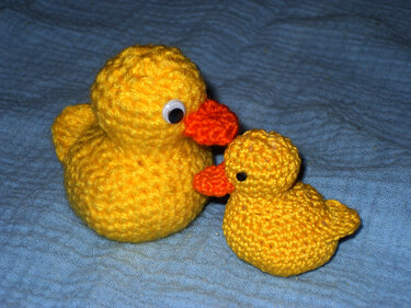 Gehäkelte gelbe Ente und Küken mit orangen Schnäbeln auf blauem Stoff