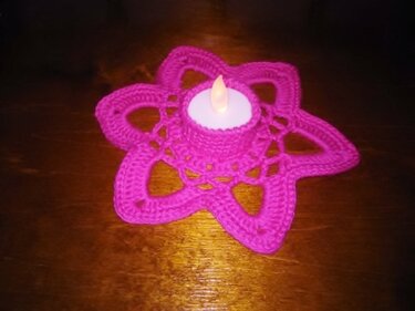 Pinkes sternförmiges Häkeldeckchen mit LED-Teelicht auf Holz