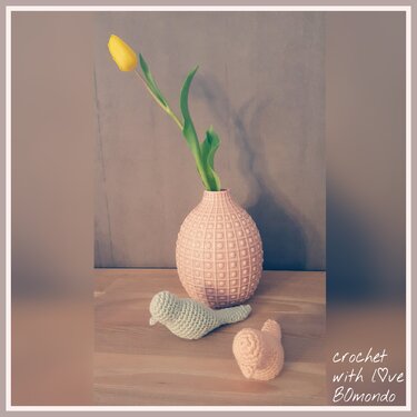 Kleine gehäkelte Vögel in Pastell neben rosa Vase mit gelber Tulpe