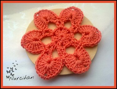 Lachsfarbener gehäkelter Untersetzer in Blumenform mit sechs Blütenblättern auf hellem Holzhintergrund.
