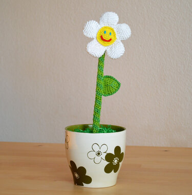 Gehäkelte weiße Margeritenblüte mit gelbem Lächeln in cremefarbenem Topf
