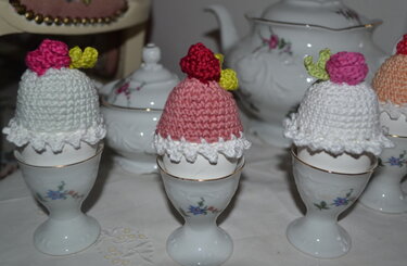 Drei gehäkelte Eierwärmer in Weiß und Rosa mit kleinen Blüten auf Porzellaneierbechern