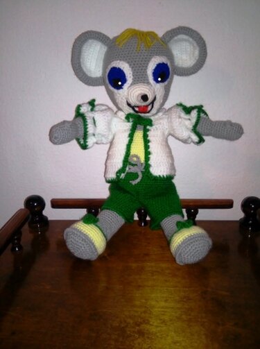 Gehäkelte graue Amigurumi‑Maus sitzend mit weißer Jacke und grüner Hose