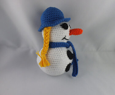 Zweigeteilter gehäkelter Amigurumi
‑Schneemann mit blauem Hut, Schal und gelbem Zopf