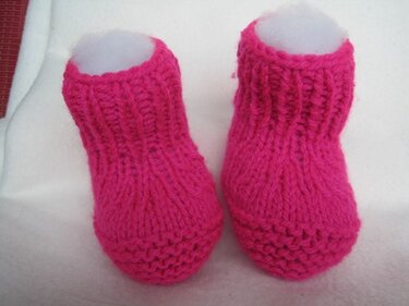 Paar pinker gestrickter Babyschuhe auf hellem Untergrund
