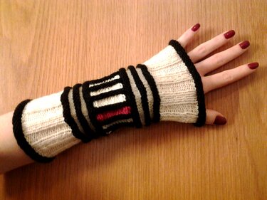 Gestrickte cremeweiße Armstulpen mit schwarzen Querstreifen und rotem Detail an einer Hand