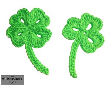 Zwei grüne, gehäkelte vierblättrige Kleeblätter auf weißem Hintergrund