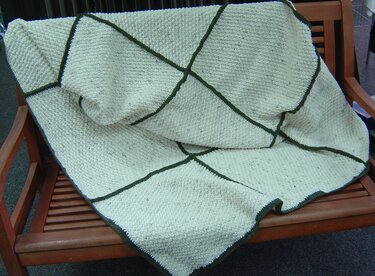 Gestrickte cremeweiße Decke mit dunkelgrünen Linien auf Holzbank