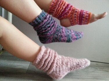 Drei Füße mit gestrickten Socken und Beinstulpen in verschiedenen Farben