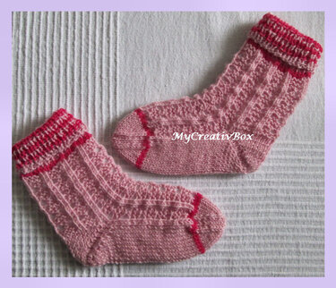 Paar handgestrickter rosa Babysocken mit Zopfmuster und roten Kontraststreifen