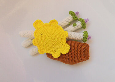 Verschiedene gehäkelte Amigurumi-Bestandteile: gelbe Blüte, weiße Stängel, braunes Körperteil