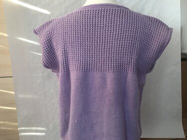 Rückansicht: ärmelloser lila Pullunder mit wabenartiger strukturierter Passe und glatt gestricktem Rumpf.