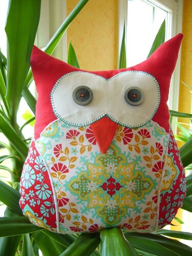 Nahaufnahme eines farbenfrohen, genähten Eulen-Kissens mit großen Knopfaugen und gemustertem Stoff am Bauch.