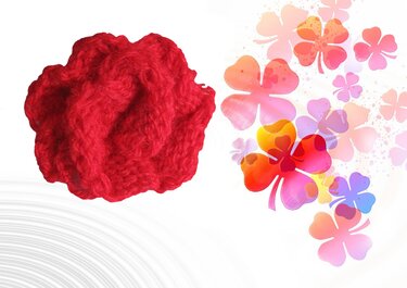 Rote gestrickte Blüte neben farbenfrohen Glückskleeblättern auf hellem Hintergrund.