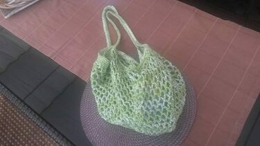 Gehäkelte hellgrüne Netztasche mit zwei Henkeln auf einem runden Platzset
