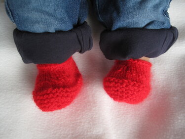 Babyfüße mit roten gestrickten Babyschuhen und umgeschlagener Jeans