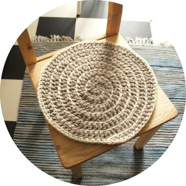 Nahaufnahme eines runden, spiralförmig gehäkelten Stuhlkissens auf einem Holzstuhl