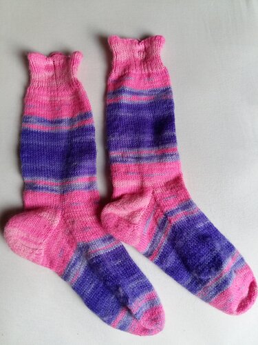 Zwei gestrickte Socken in Pink- und Lilatönen mit Streifen und Rüschenbündchen