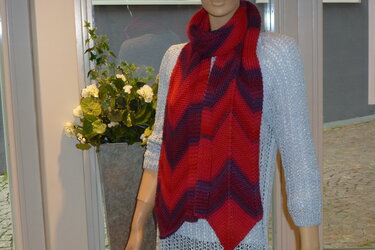 Mannequin trägt rot-violett gestreiften Chevron-Schal über hellgrauem Pullover