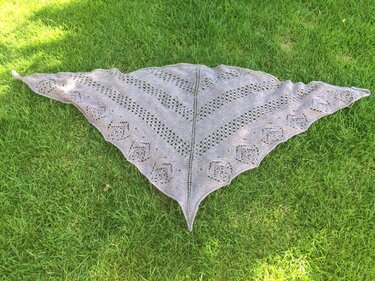 Hellgraues gestricktes Dreieckstuch mit Lochmuster und Zierkante auf grünem Rasen