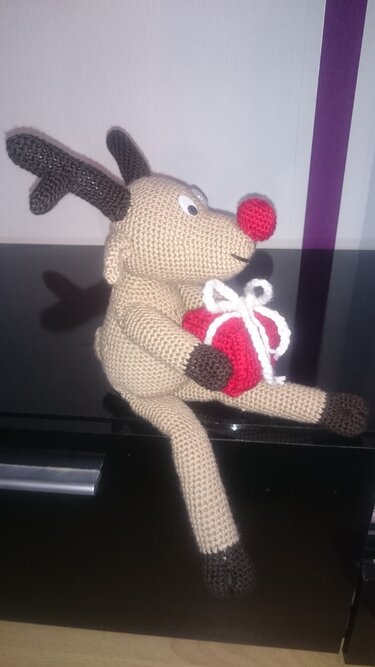 Sitzendes gehäkeltes Rentier-Amigurumi hält rotes Geschenk mit weißer Schleife